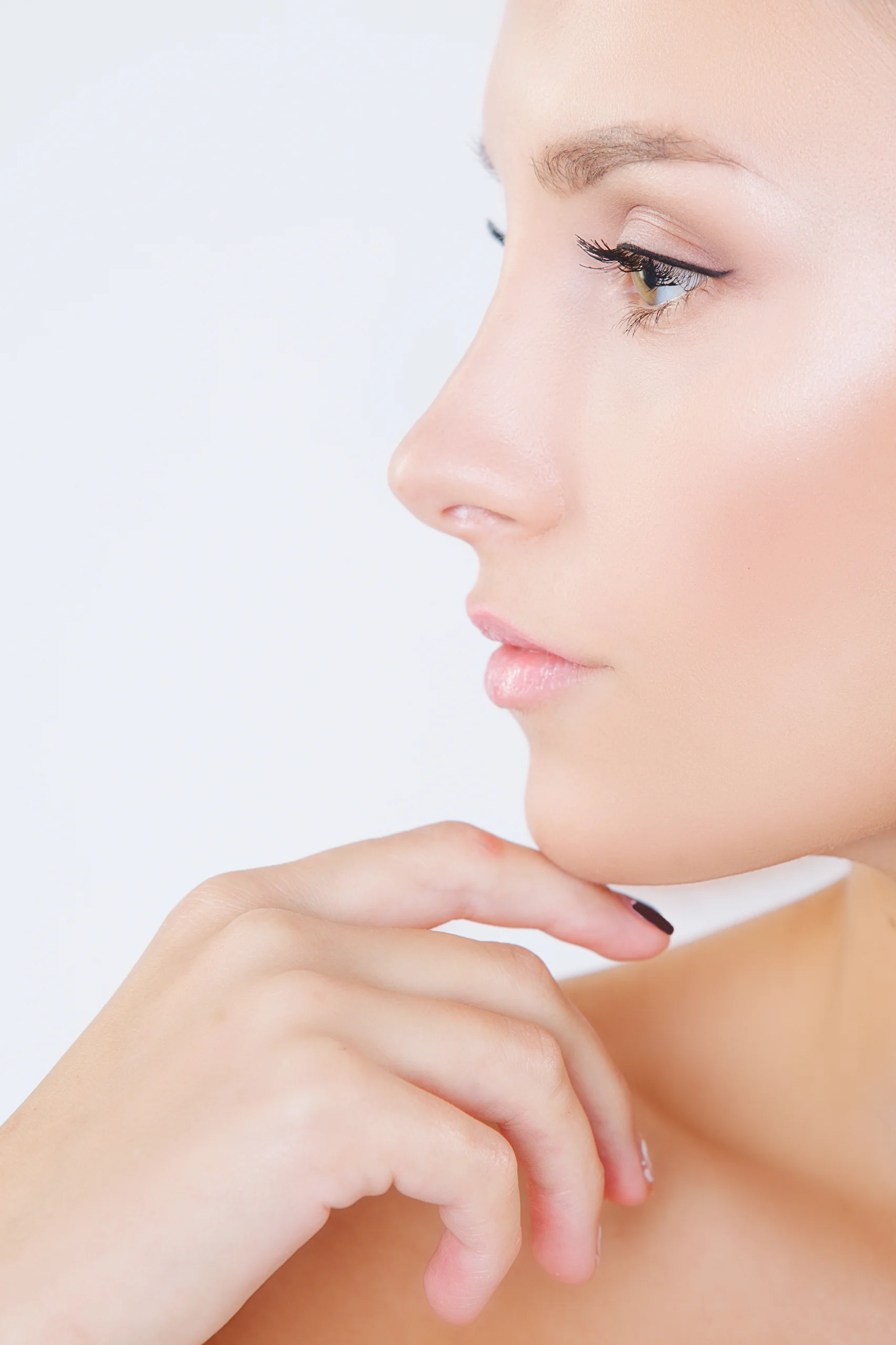 A front-facing portrait of a woman pointing to her nasal tip, representing an ideal candidate for Rhinoplasty Tip Reshaping.