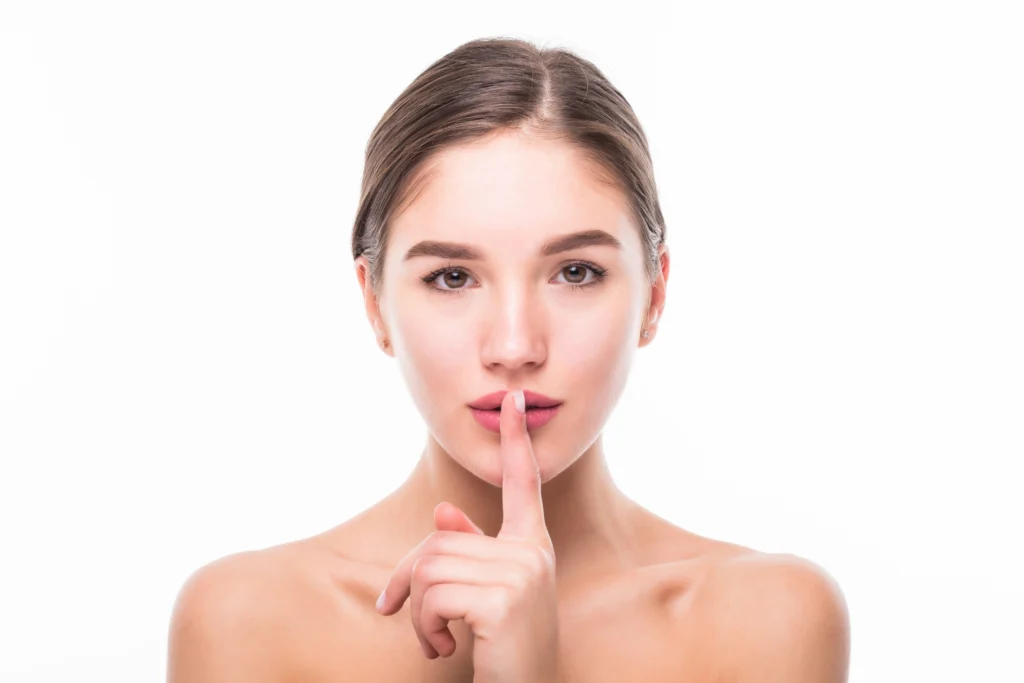 A woman holding a finger to her lips to represent the subtle and natural-looking results of Rhinoplasty Tip Reshaping.