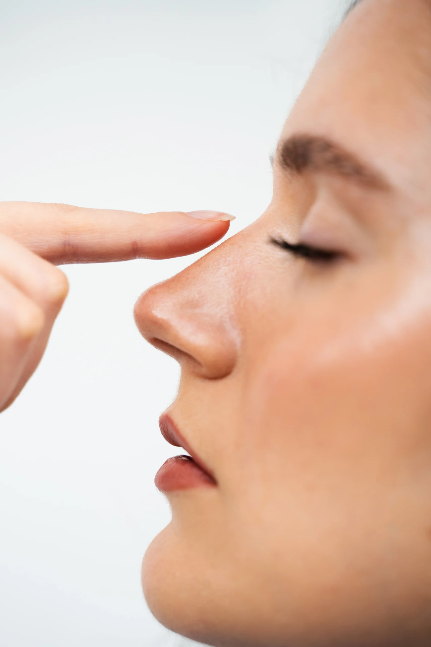A close-up profile view of a woman pointing to her nasal bridge to identify different types of Septoplasty corrections.