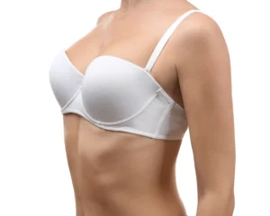 A side profile view of a woman's torso wearing a white bra against a white background, highlighting the projected upper-pole fullness and silhouette achieved through a breast implant procedure.