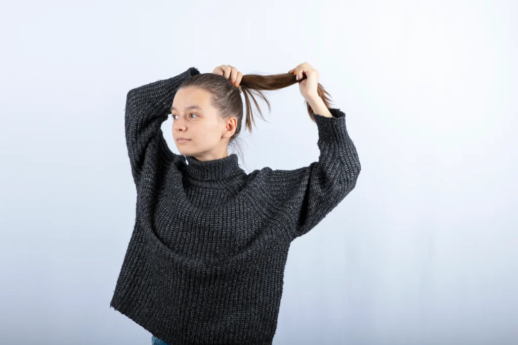 Young woman in a grey sweater tying her hair into a ponytail to show improved density after a hair transplant in Dubai.