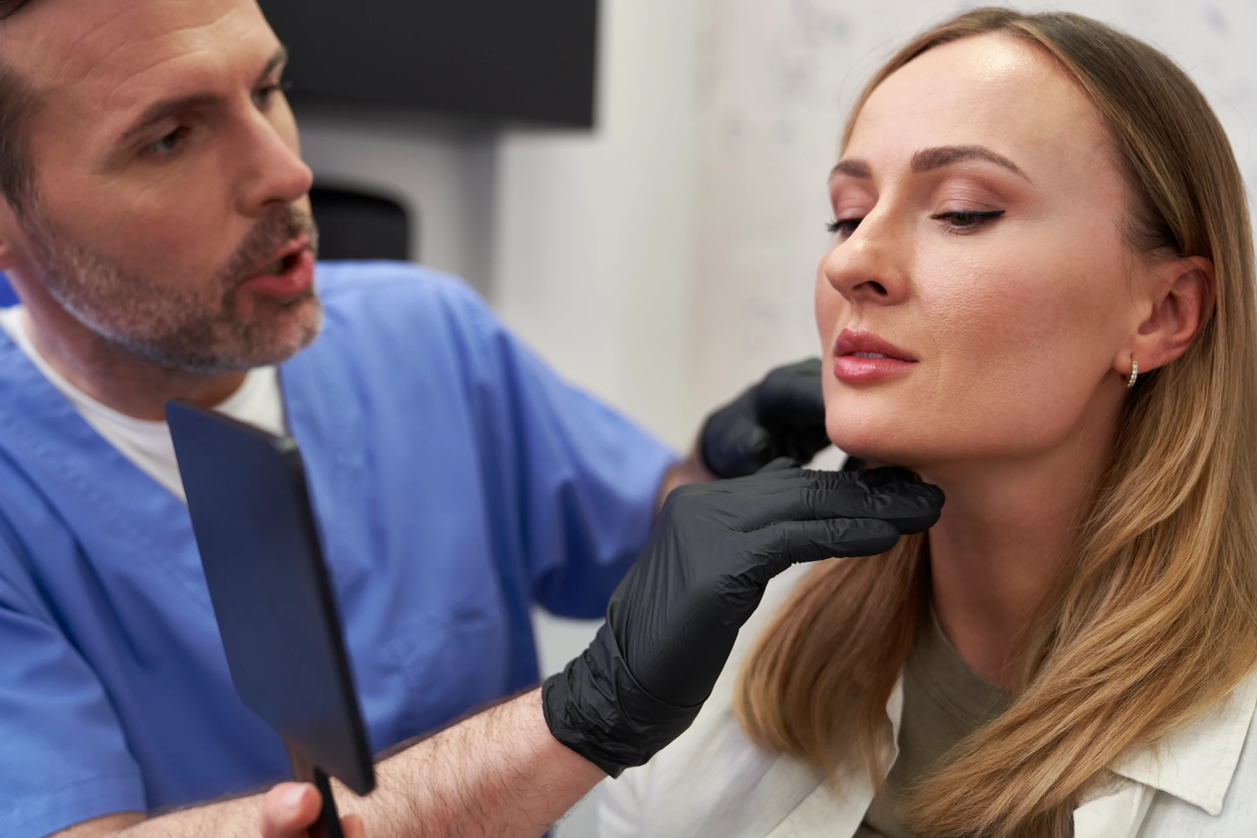 A close-up view of a surgeon's hand in a white glove using a black pen to draw a curved surgical guide line directly under a woman's nose to explain How long do lip lifts last.