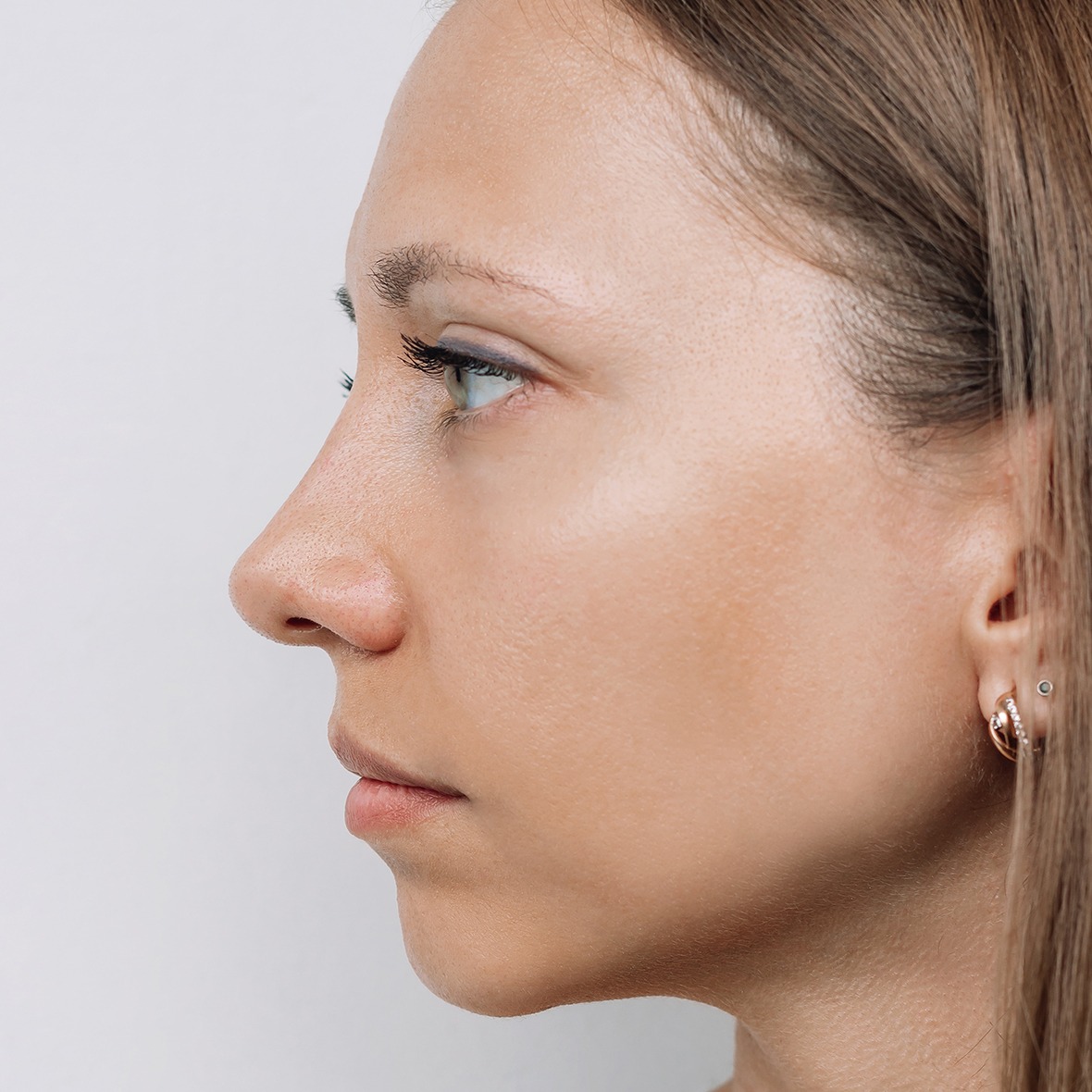 A close-up side profile shot of a woman's face from the forehead to the chin looking forward against a plain white background, showcasing a smooth, straight nasal bridge and an elevated, naturally contoured nasal tip achieved after a Rhinoplasty in Dubai.
