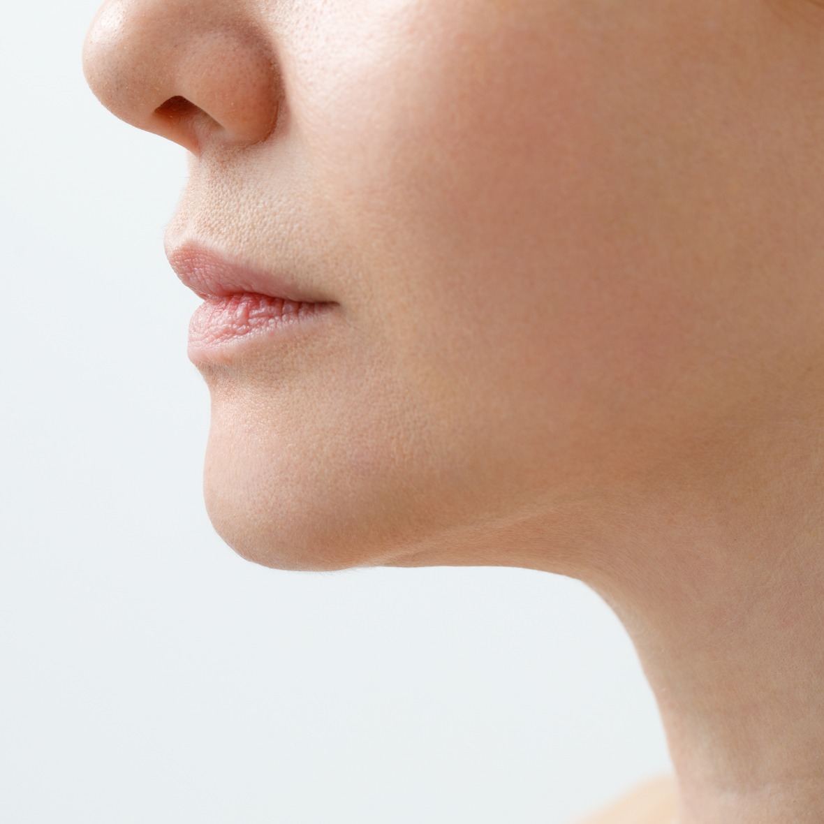 A close-up three-quarters side profile view of a person's lower face, lips, jawline, and neck against a plain white background, showcasing a streamlined cheek profile and reduced mid-face volume achieved after Buccal Fat Removal in Dubai.