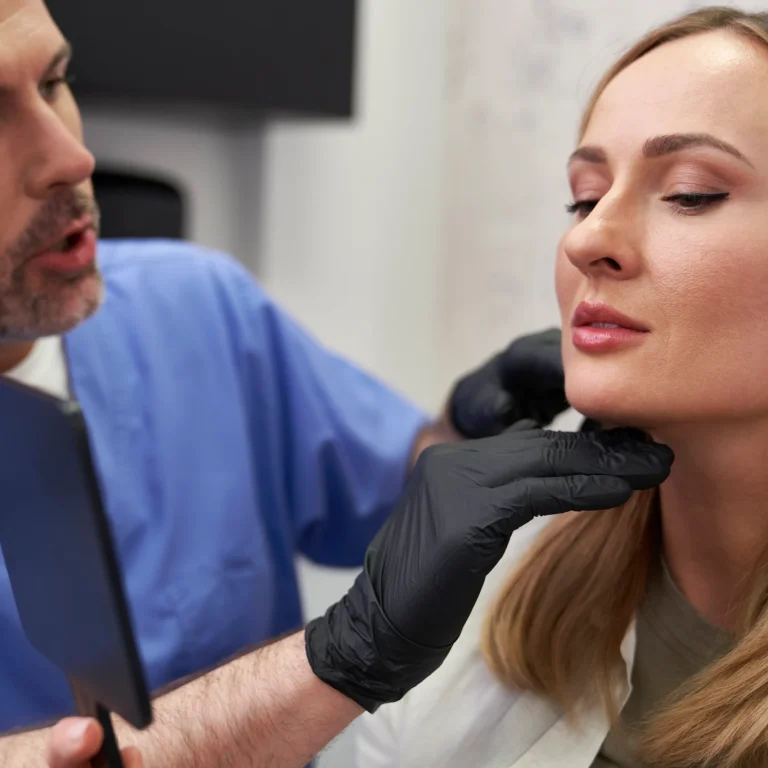 A close-up view of a surgeon's hand in a white glove using a black pen to draw a curved surgical guide line directly under a woman's nose to explain How long do lip lifts last.